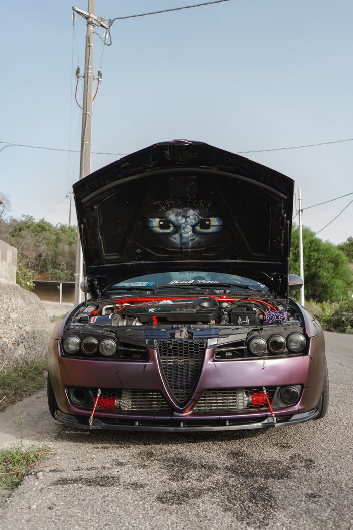 Front view of a customized car with its hood open, showcasing the engine and artistic graphic.