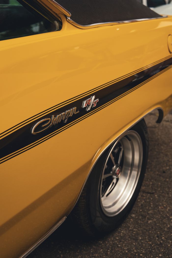 Side view of a classic yellow muscle car with a black stripe and chrome wheel, showcasing vintage automotive design.